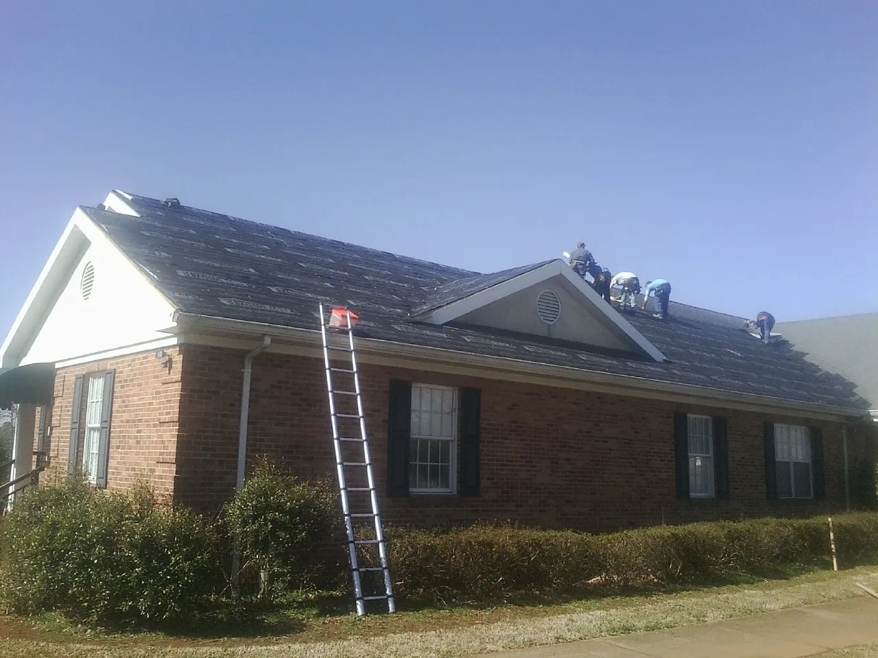 Crew tearing shingles off a brick ranch roof with a ladder set — Emergency Roof Repair work by our crew in Leesville