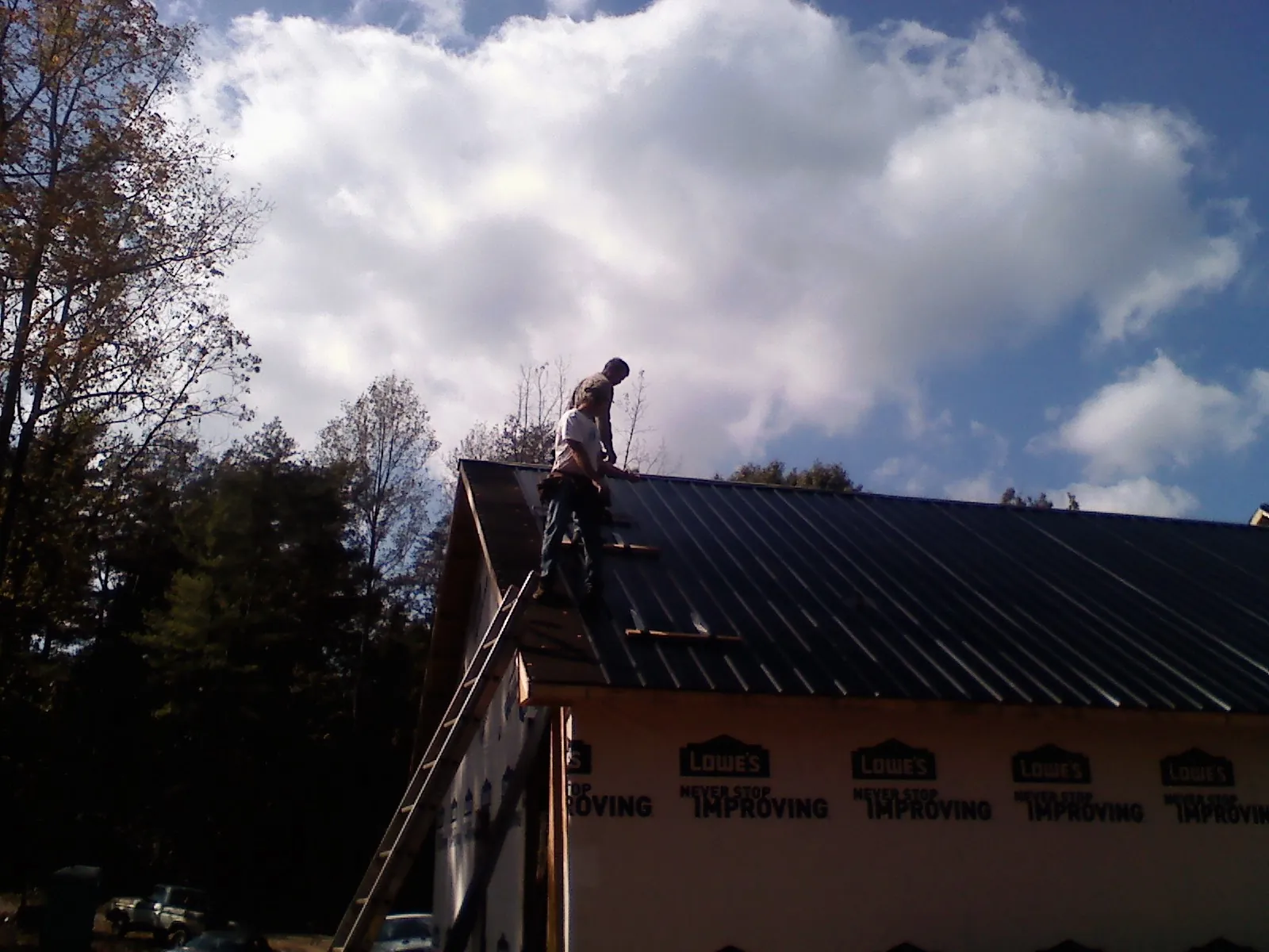 Roofer fastening dark metal panels high against a cloudy sky, from a Roof Inspection job in Leesville